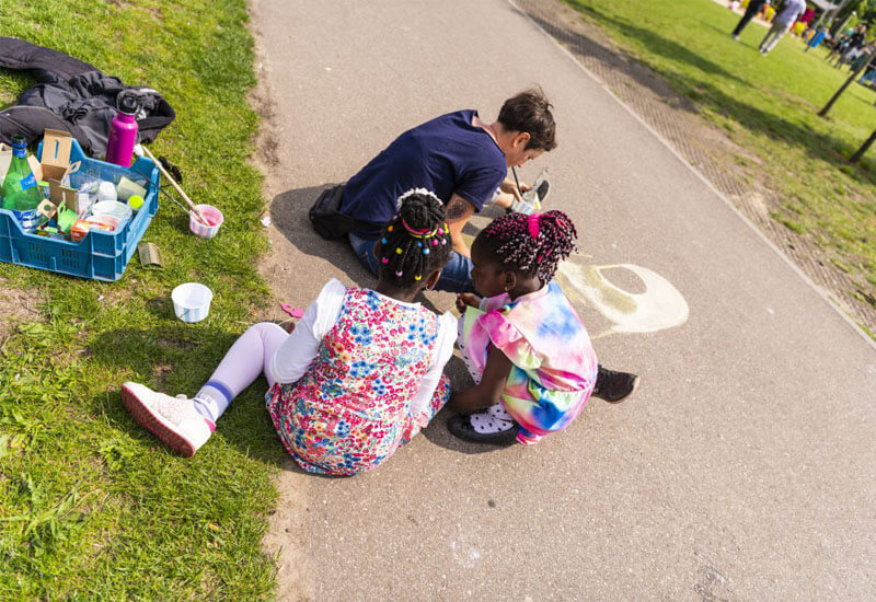Twee kinderen kijken zittend toe hoe een artiest de straat beschildert op het Vergezichtenfestival.
